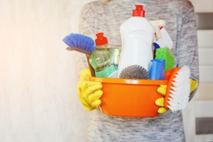 Woman hands holding tub with supplies for house cleaning.