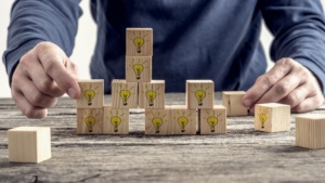 Front view of a man arranging wooden blocks with hand drawn yellow lightbulb in a random structure. Conceptual of research, education and innovation.